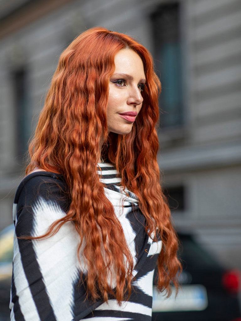 Loose perm: Side view of a woman with long auburn hair with layered loose perm hairstyle starting from above the ears