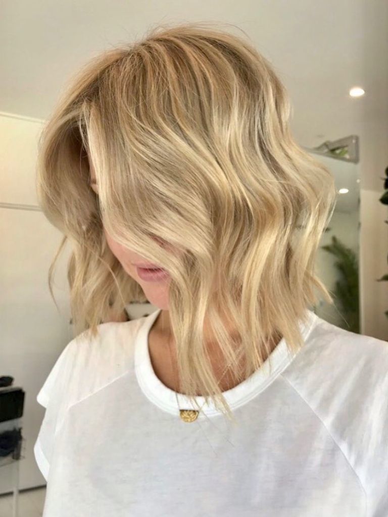 Woman with wavy honey blonde choppy bob wearing a white t-shirt.