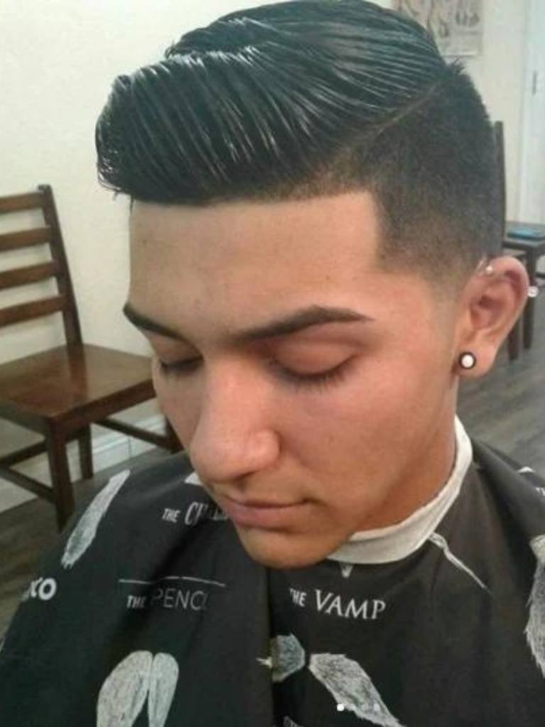 photo from above of a brunette man in the barbers chair with a quiffed up taper comb over hair cut styled with wet look gel