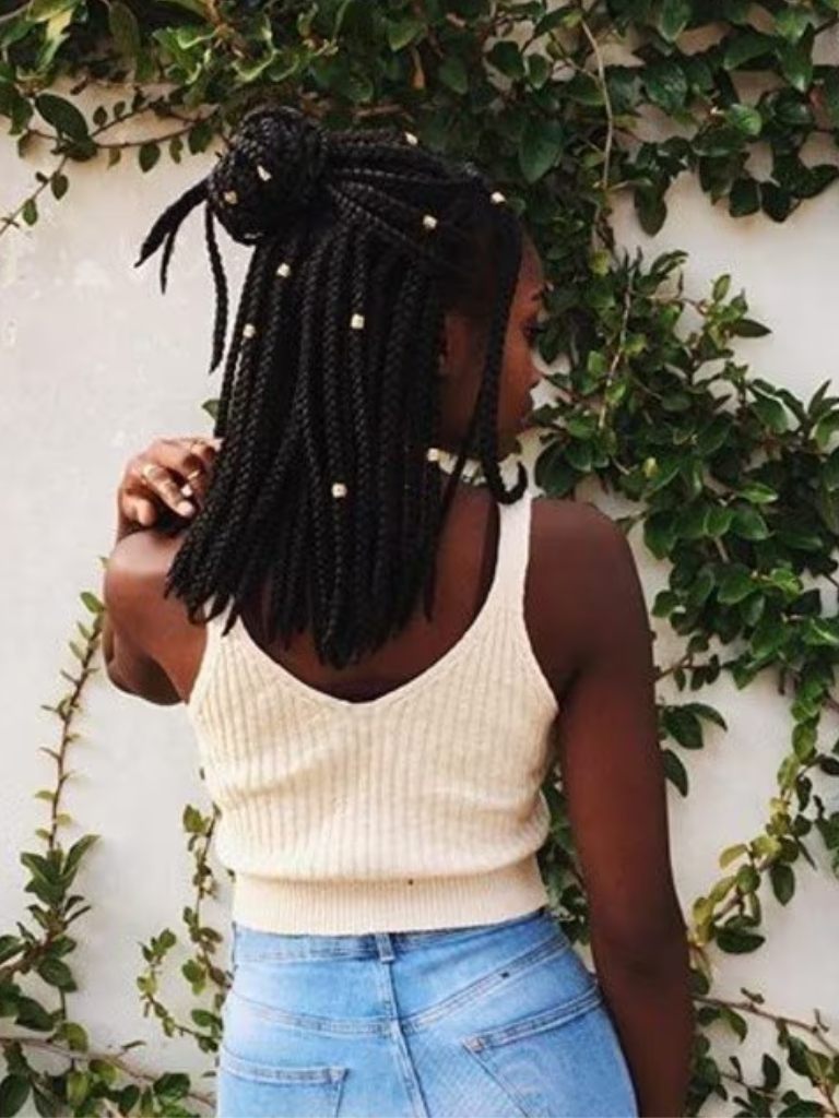 backshot of woman with medium sized box braids styled into a half up half down bun hairstyle
