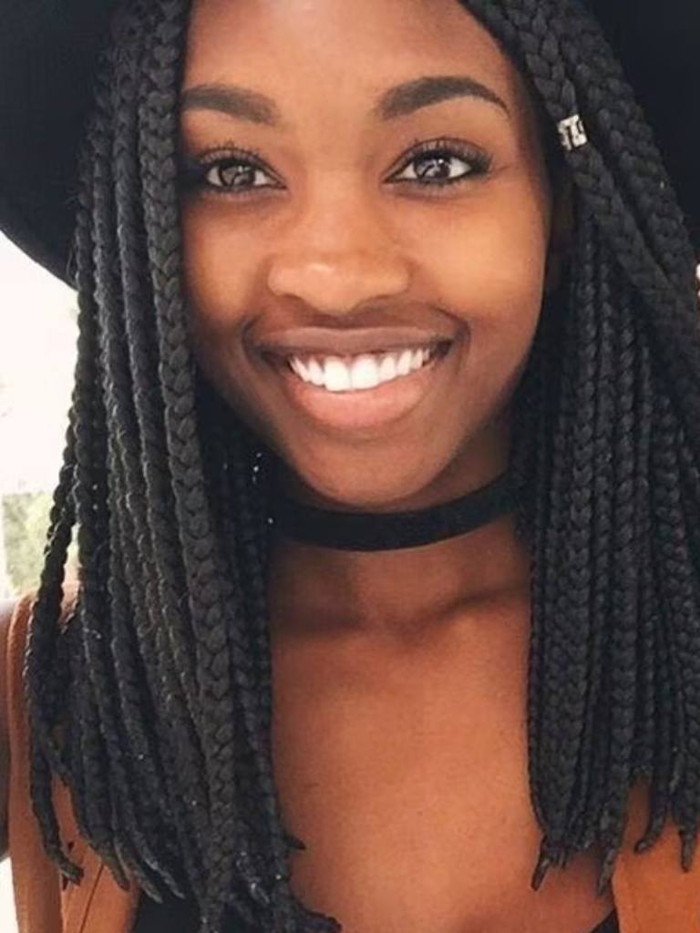 medium box braids hairstyles: shot of woman with medium box braids wearing hat and smiling