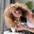 Girls with big frizzy loose permed hair leaning into sunlight cuddling cat