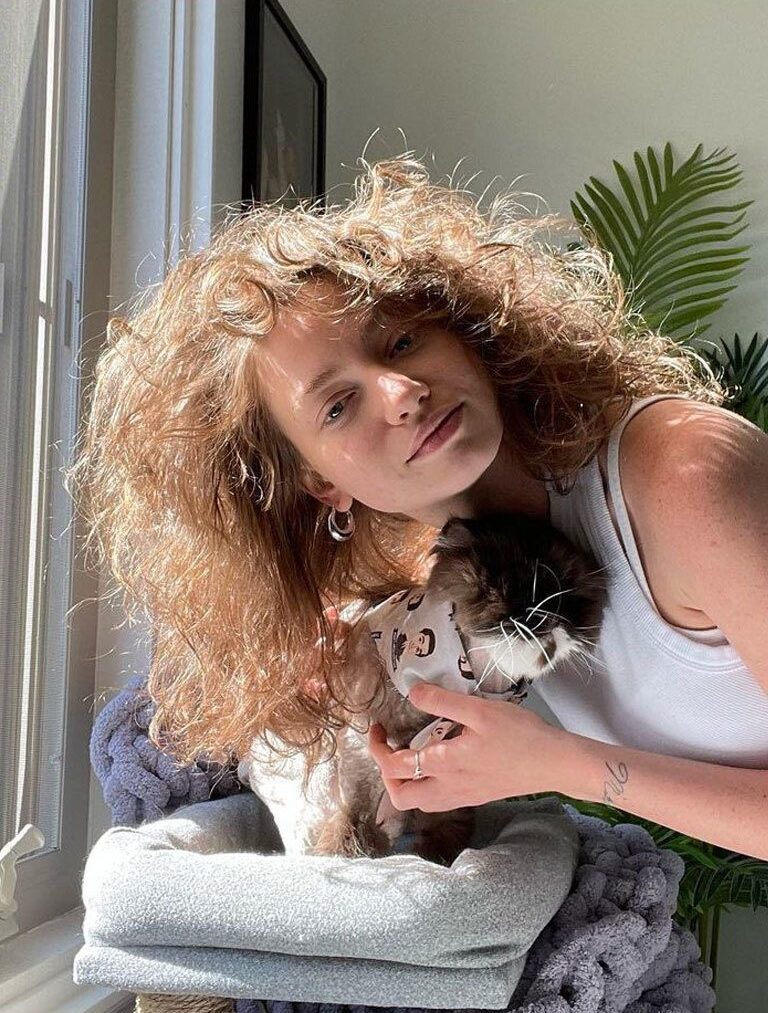 Girls with big frizzy loose permed hair leaning into sunlight cuddling cat