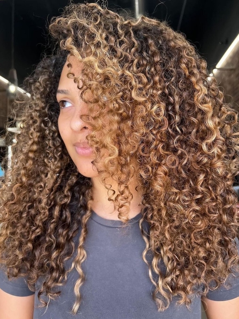 Woman with long curly hair and honey blond balayage