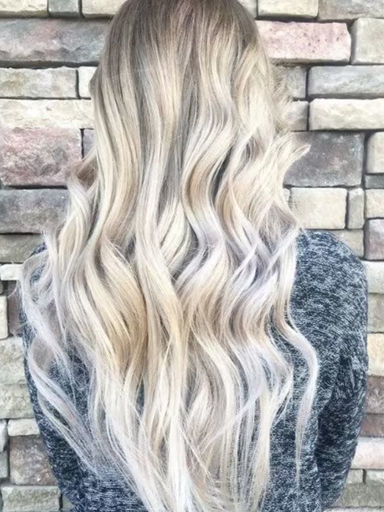 Back view of a woman with long wavy platinum ash blonde hair, wearing grey