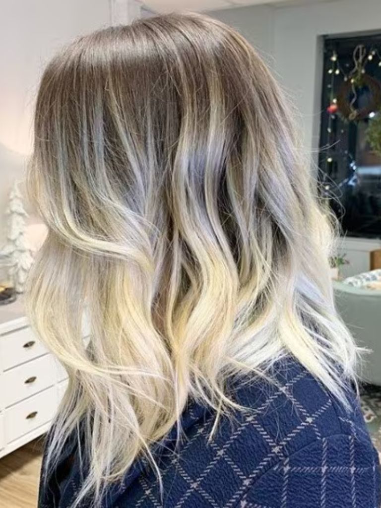 Side view of a woman with mid-length brown to blonde sombre hair styled in soft waves, wearing a shirt