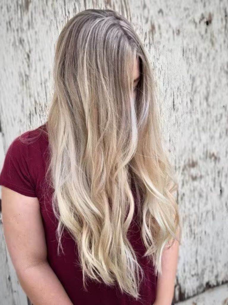 Photo of a woman with long vanilla blonde wavy hair, wearing a maroon t-shirt