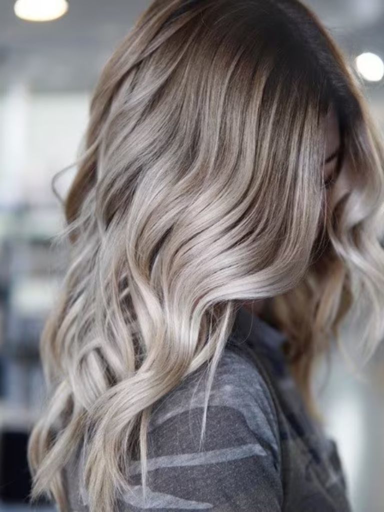 Close-up of a woman with wavy ash blonde hair with grey shadow roots