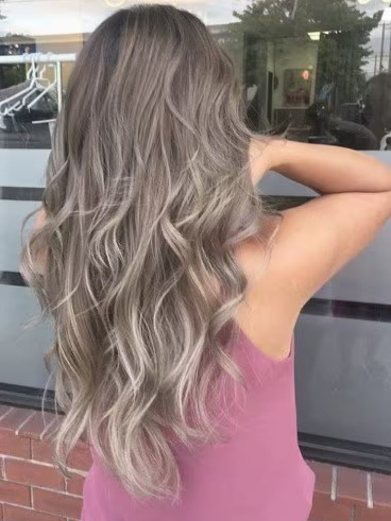 Back view of a woman with long silvery ash grey curly hair, wearing a lilac top