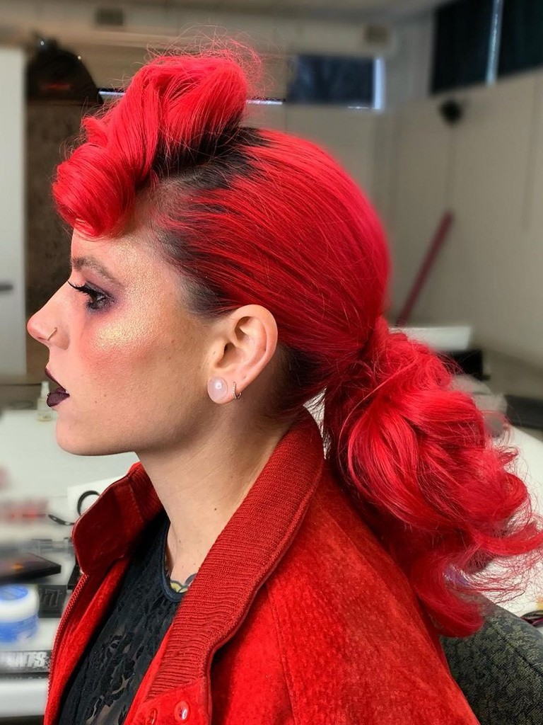 Woman in profile with bright pillarbox red hair and dark roots styled in pompadour and ponytail