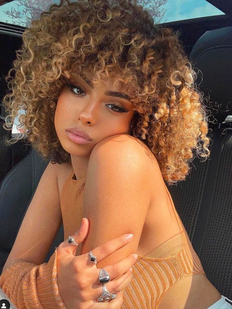 Woman with very curly hair in a long mushroom cut with blonde highlights