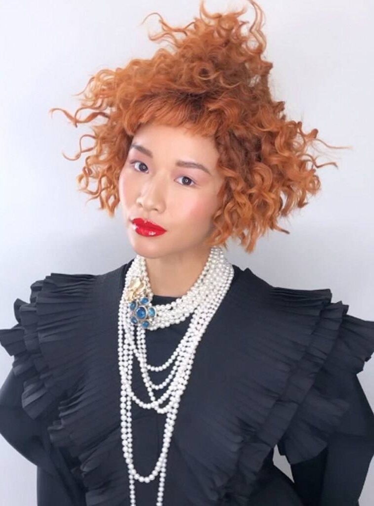 Asian woman with red hair with curls cropped in different length, piled in her head, with short fringe