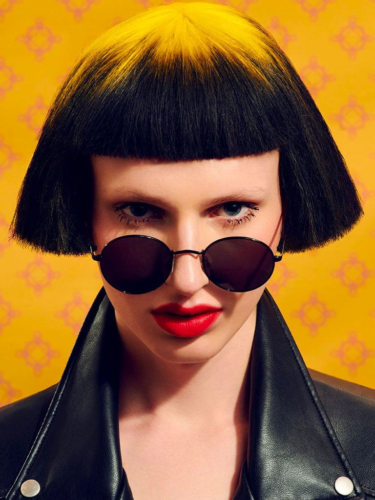 woman with mushroom cut with blunt ends and fringe. Yellow tinted crown on dark brown hair