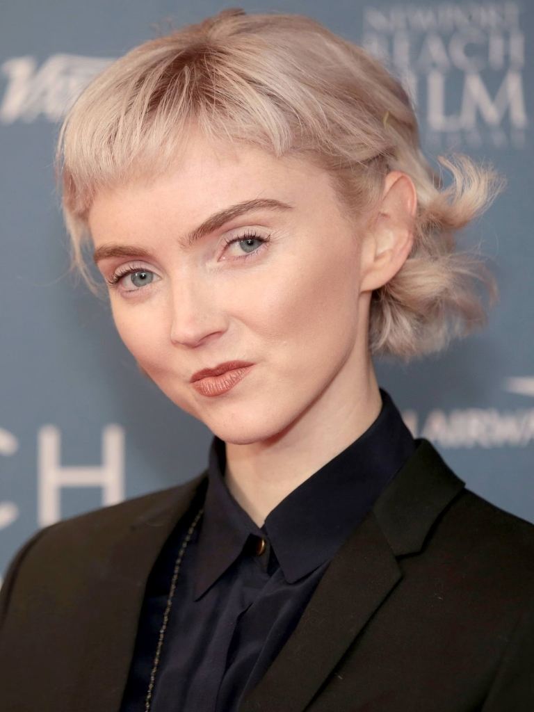 Short bangs: Lily Cole with bleach blonde curly short hair with short baby bangs wearing a black top.