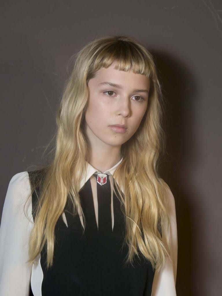 Short bangs: Woman with long blonde wavy hair with short micro fringe wearing a white shirt.
