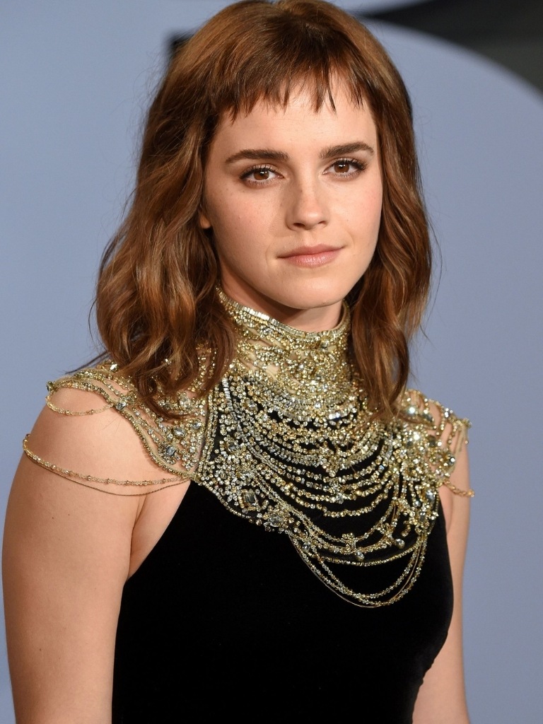 Short bangs: Emma Watson with shoulder length wavy brown hair with short micro fringe wearing a black dress with chain neckline.