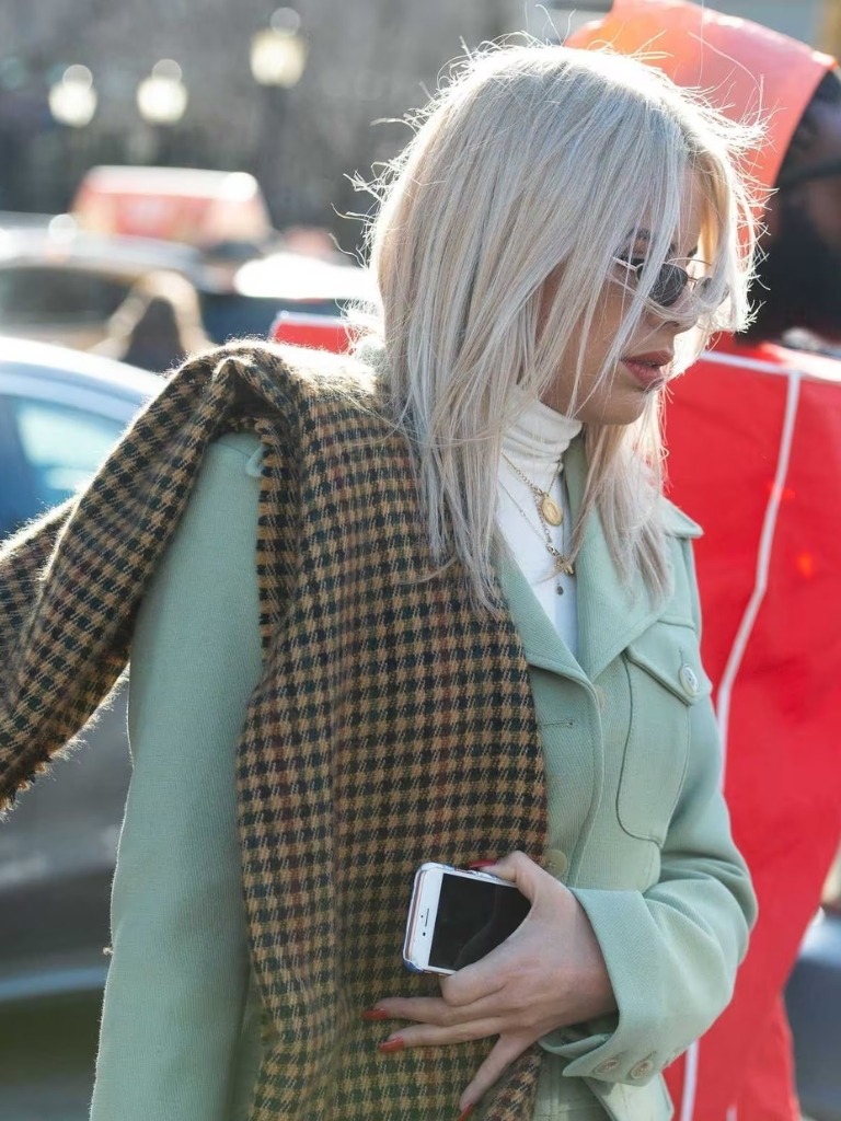 Woman with ash white hair in a green coat and scarf