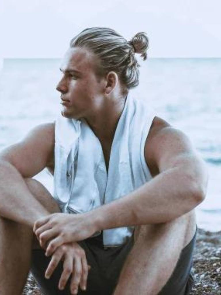 Viking Hairstyles: Man sitting on the beach with blonde hair in a man bun
