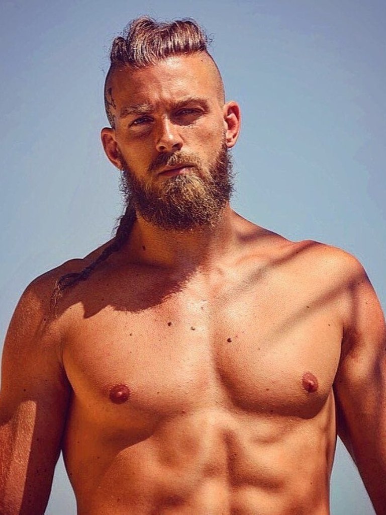 Viking Hairstyles: Man with swept back hair styled into skinny braid, with rugged beard on the beach