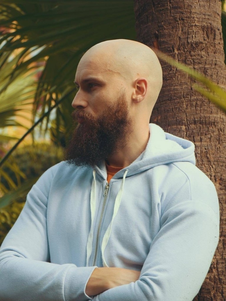 Viking hairstyles: Shot of man with bald head with Viking messy beard posing against tree