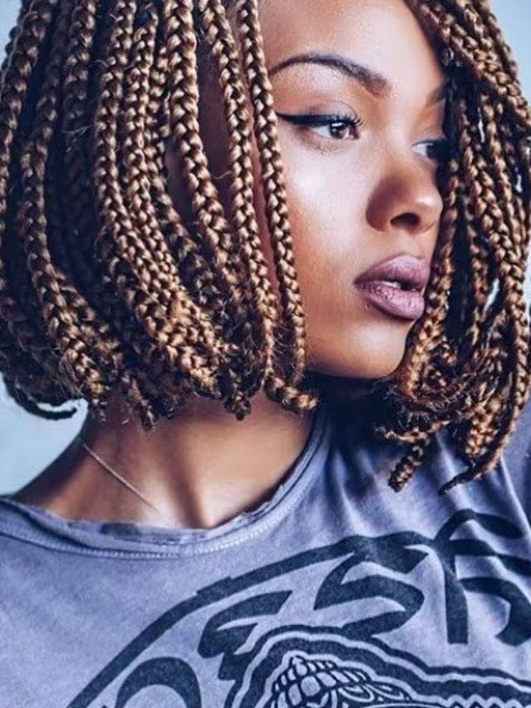 Box braids bob: Woman with caramel brown short bob box braids hairstyle, wearing a grey top