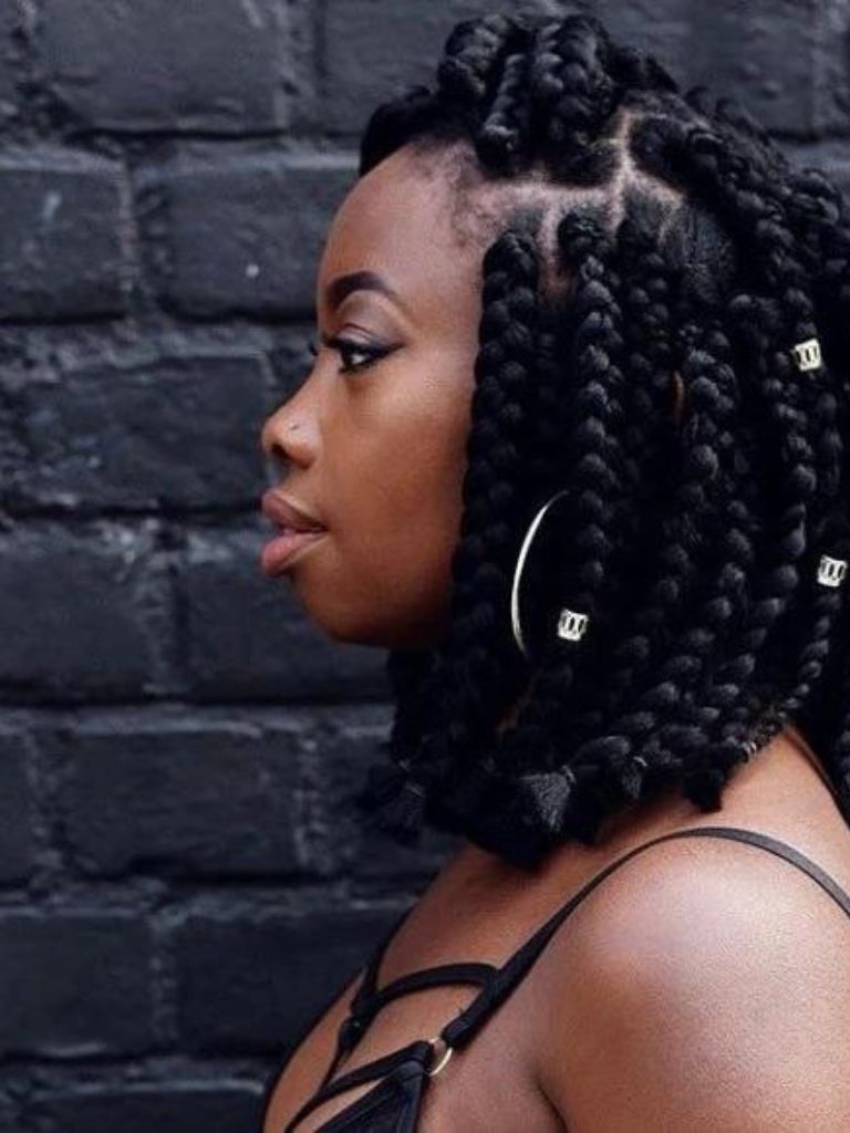 Box braids bob: Woman with dark brown thick, short dookie braids with hair cuffs in them, wearing a black top and posing against a brick wall
