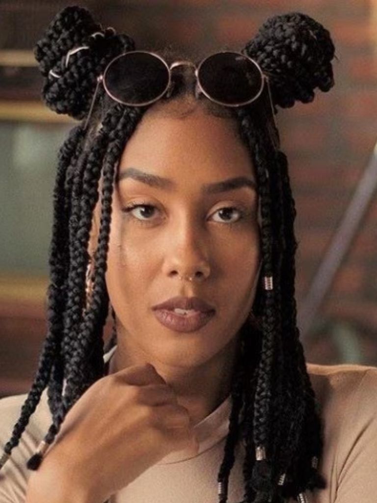 Bob braids bob: Woman with dark brown short box braids styled into half-up, half-down space buns, wearing round sunglasses and beige turtleneck top