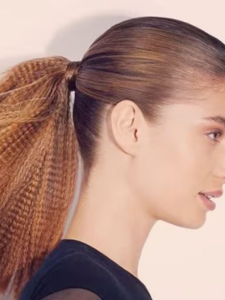 Crimped hair: Woman with dark blonde hair in ponytail with crimped ends wearing a black top.