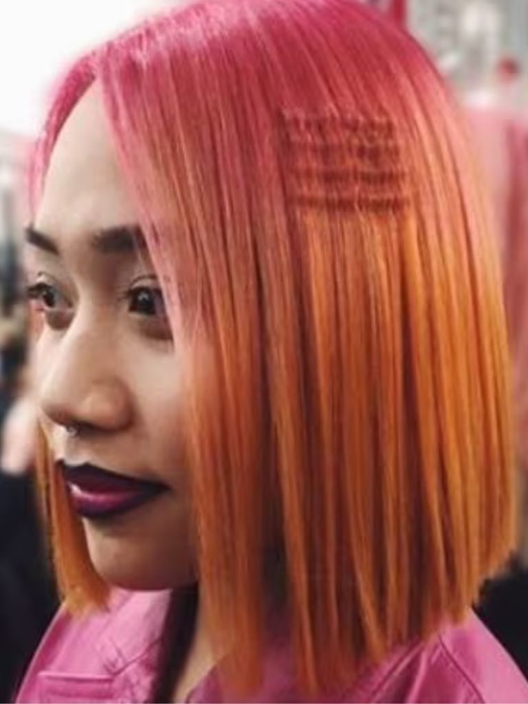 Crimped hair: Woman with a pink and orange ombre straight bob with single crimped section.