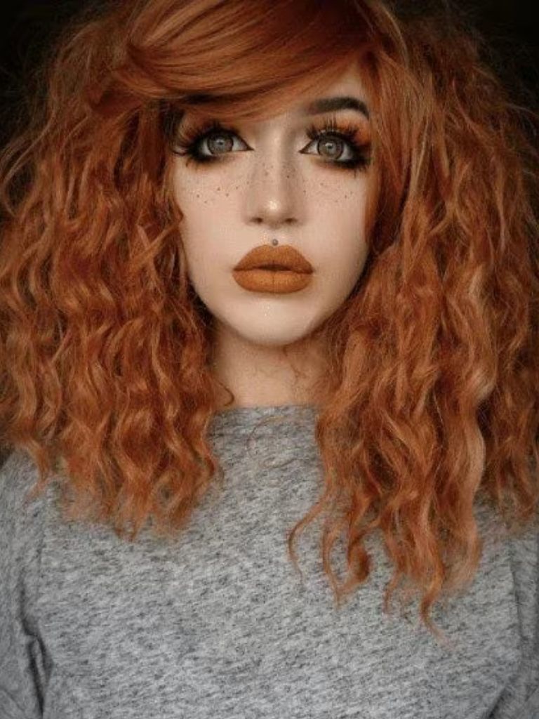 Crimped hair: Woman with copper red medium length hair in crimped waves with full side fringe wearing a grey top.