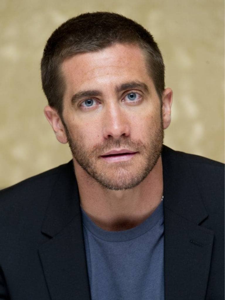 Hairstyles for receding hairline: Headshot of Jake Gyllenhaal with a crew cut haircut, wearing a blue t-shirt and black blazer