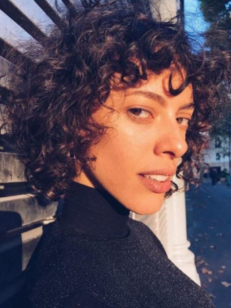 Woman with short brown curly hair with a fringe