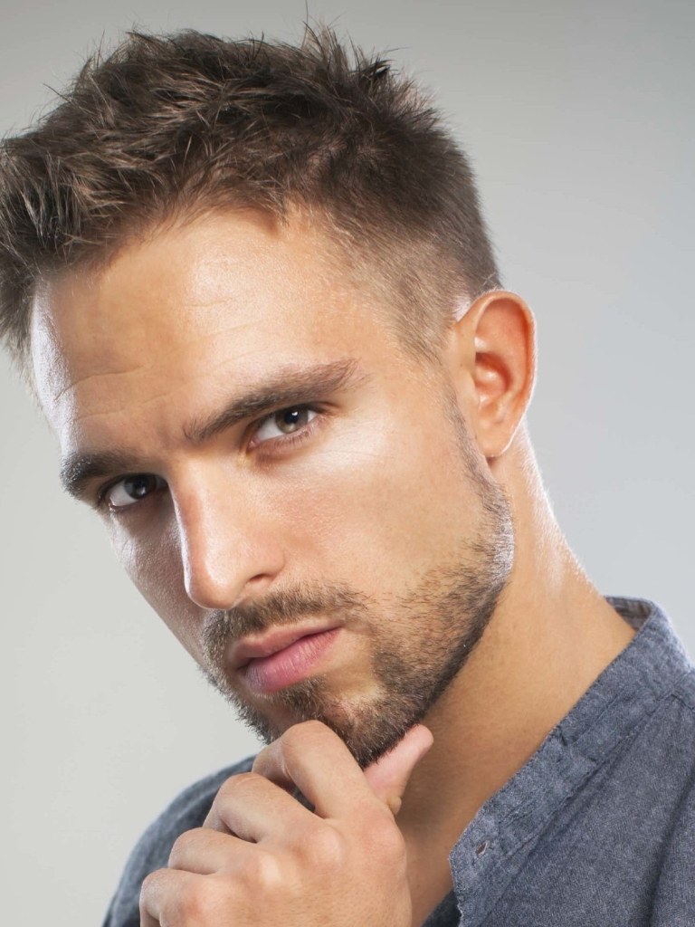 Men's haircuts for round faces: A man with a short, jagged hairstyle, wearing grey top and posing in studio