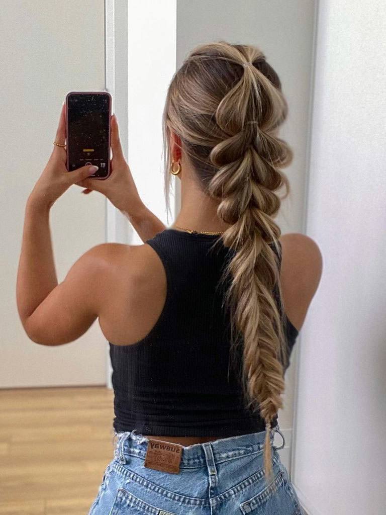 Woman with long blonde hair seen from behind. Wearing a pull-through fishtail braid