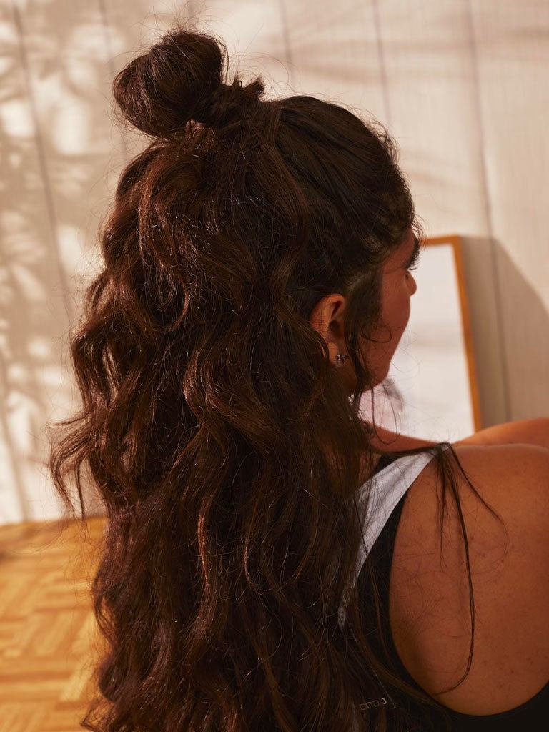 Woman with long dark hair styled into a half-up bun