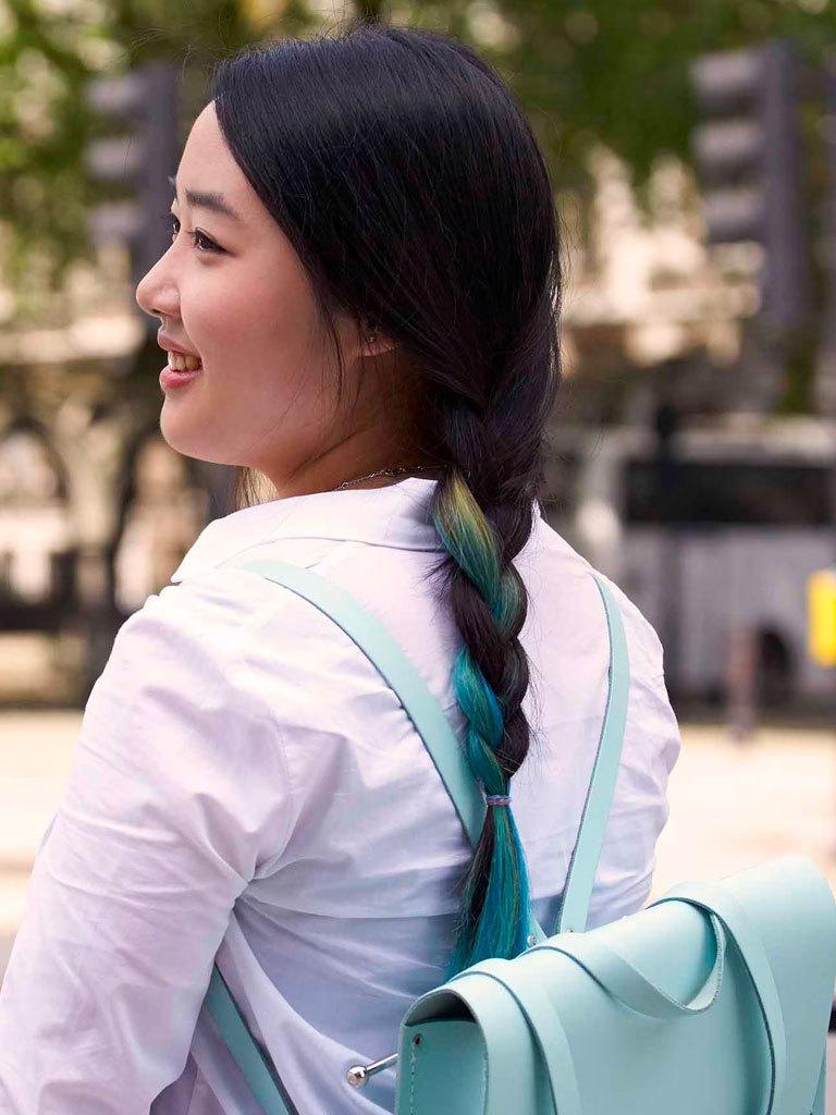 Easy hairstyles for long hair: Woman with long dark brown hair with blue highlight styled in a braid wearing a light blue backpack.