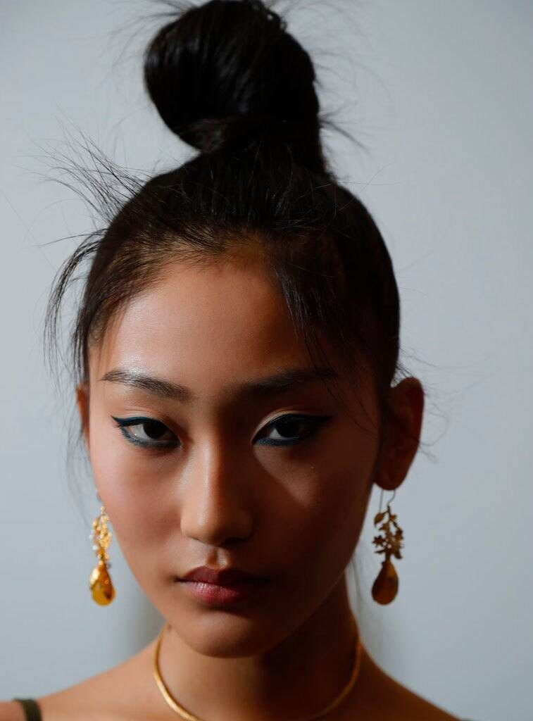 Easy hairstyles for long hair: Woman with dark brown straight hair in a high topknot bun wearing dangling earrings.