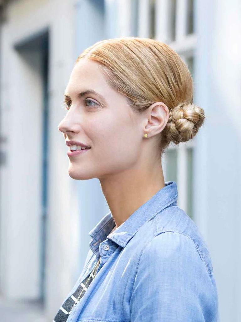 close up shot of woman outside with braided low macaron bun hairstyles, wearing denim and sporty clothing