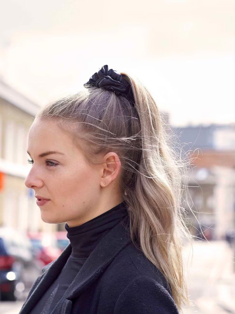 Easy hairstyles for long hair: Woman with blonde highlighted wavy hair in high ponytail with a black scrunchie wearing a black rollneck top and blazer.