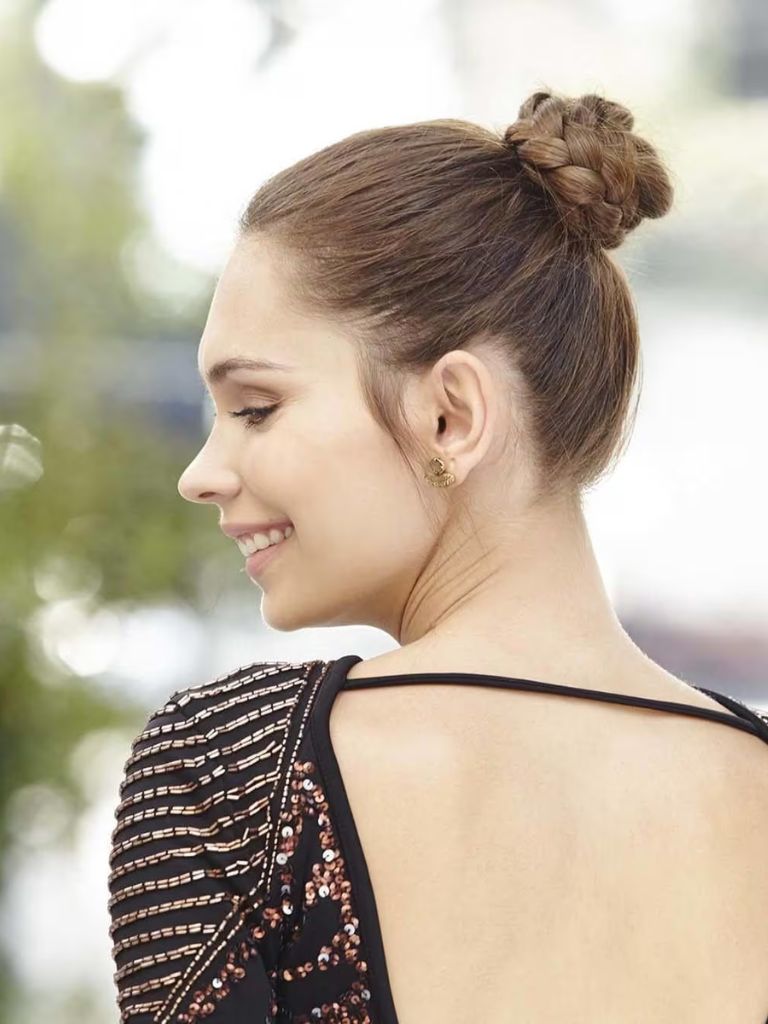 Updos with braids: Close up shot of a woman with medium brown hair styled into a braided topknot.