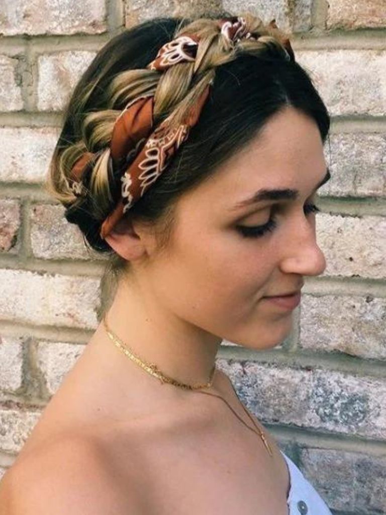 Updos with braids: Close up shot of a woman with caramel brown hair styled into a milkmaid braid updo with a scarf accessory.