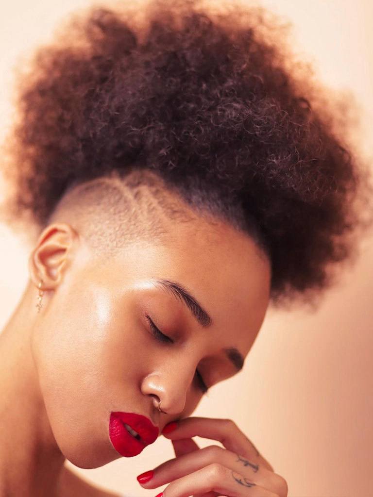 Woman with high Afro with shaved side and decorative detail. Wearing red lips and nails