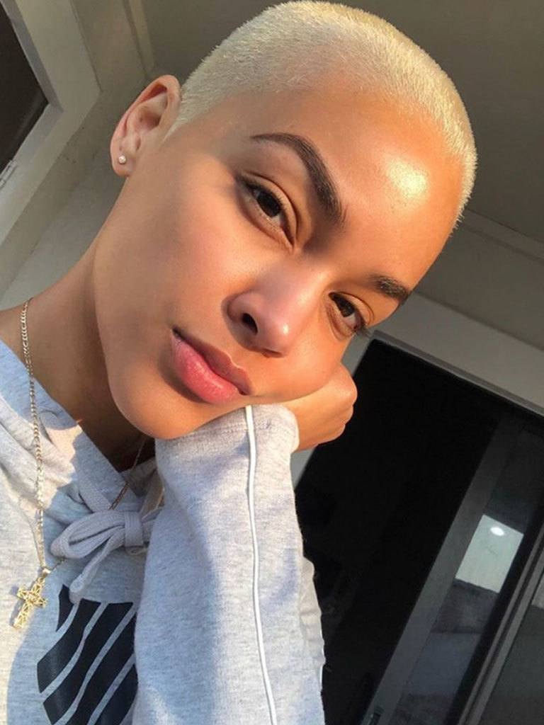 Woman looking at camera. Wearing a bleached buzzcut shaved hairstyle.