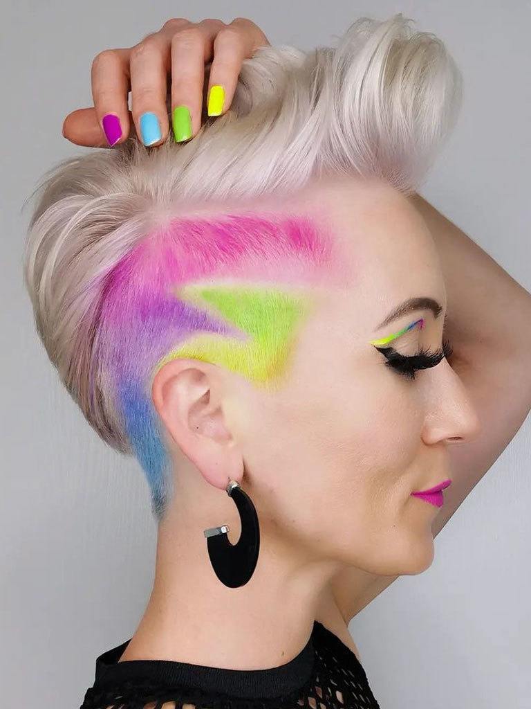 Woman in profile with pompadour hairstyle with shaved sides with decorative detail in bright colours. Matching colours on nails and eyes