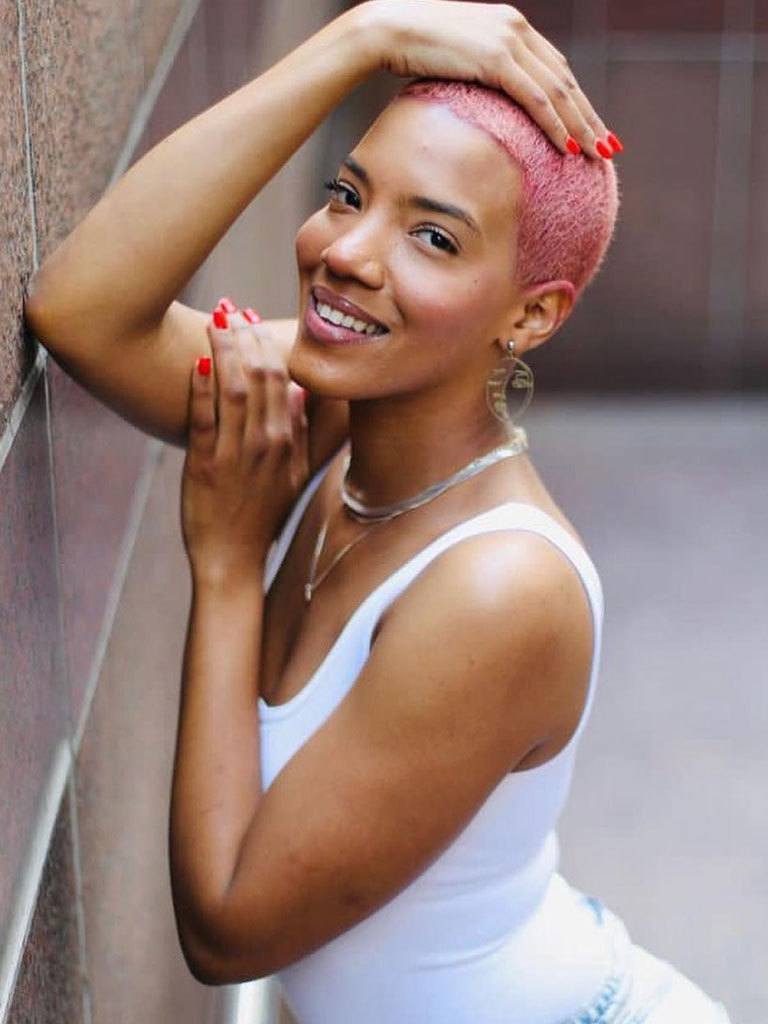 Woman with pink buzzcut hair smiling at camera