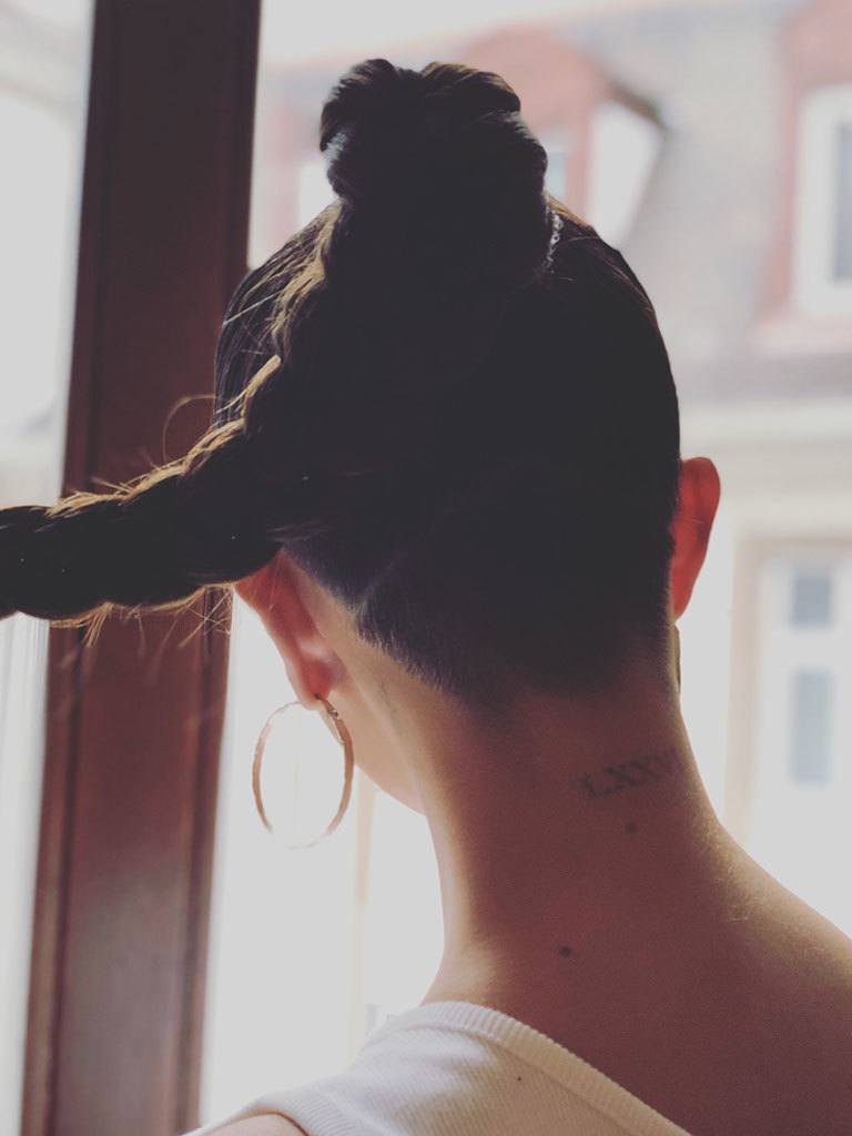 Selena Gomez with shaved back and dark hair styled into a swinging ponytail