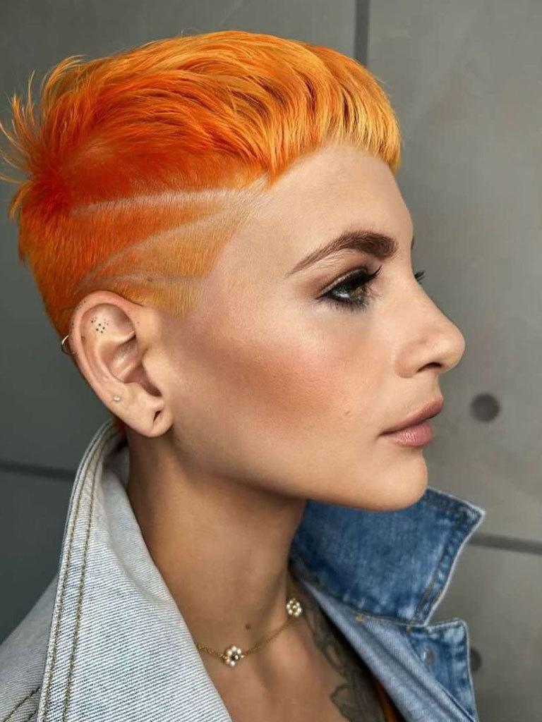 Women with hair in a French crop style, with shaved sides with decorative detail. Colour is balayage orange
