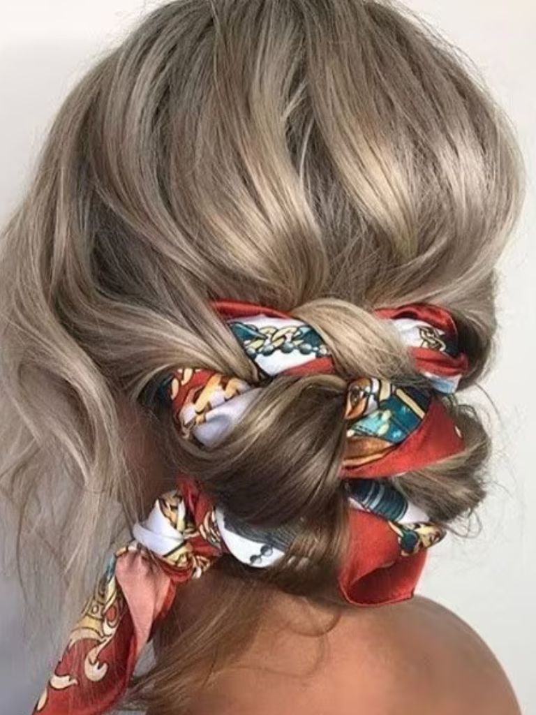 Updos with braids: Back shot of a woman with ash blonde hair styled into a scarf braided low bun hairstyle.