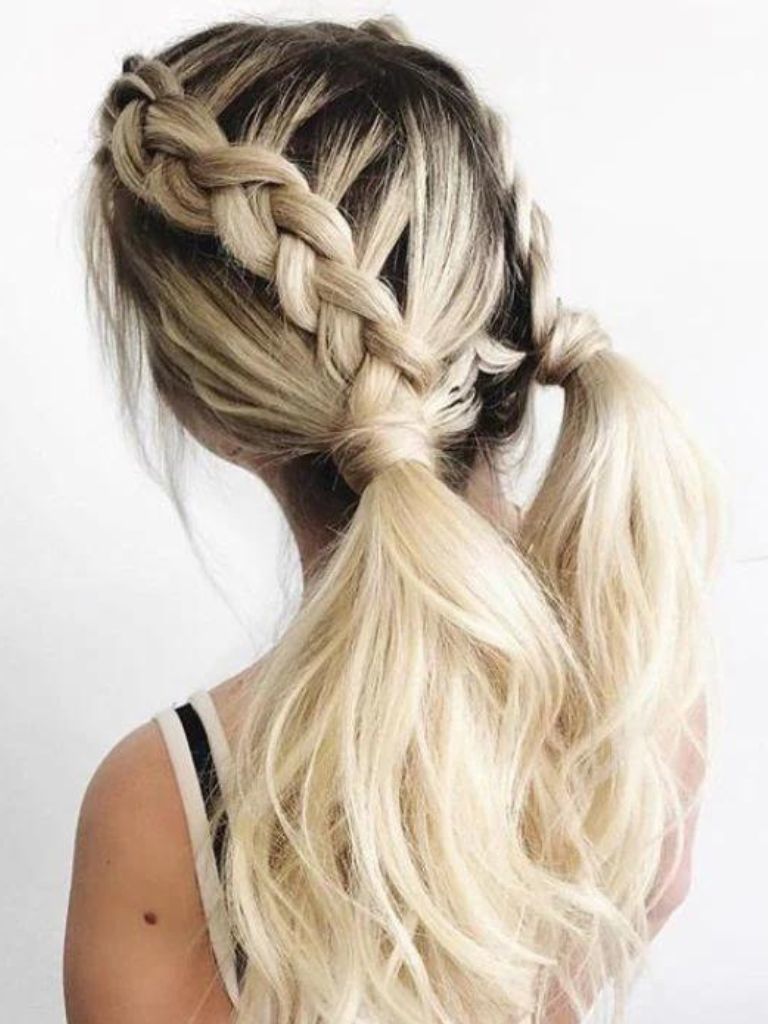 Updos with braids: Back shot of a woman with bleach blonde hair styled into Dutch braid pigtails into ponytails.
