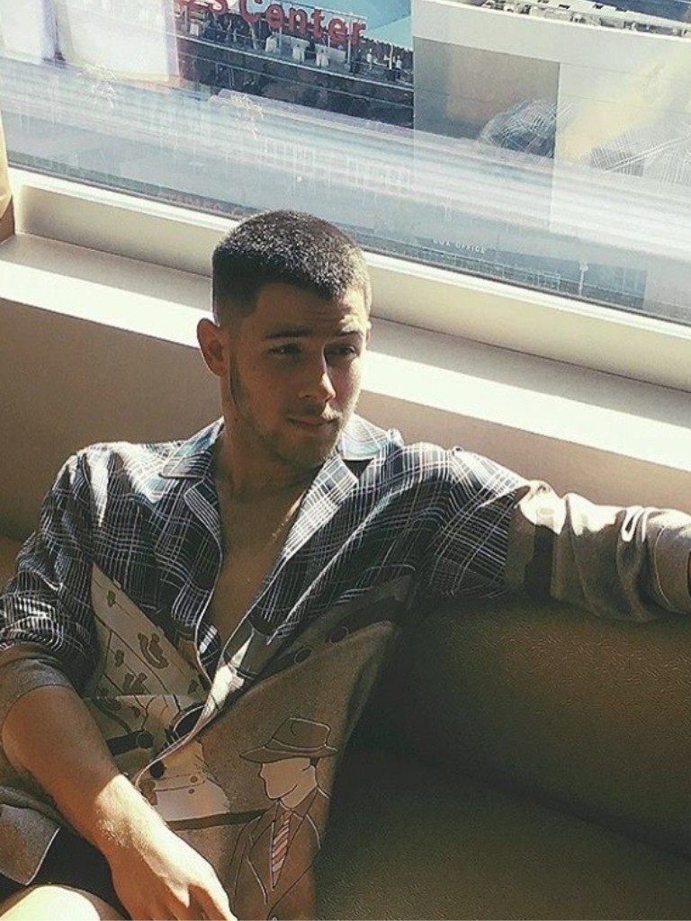 nick jonas in a plaid shirt holding a drink with short buzz cut hair